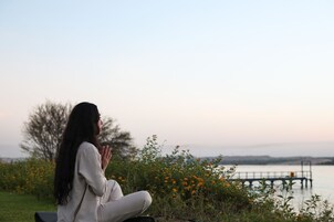Una persona sentada al aire libre, con un cuerpo de agua y un puente al fondo.