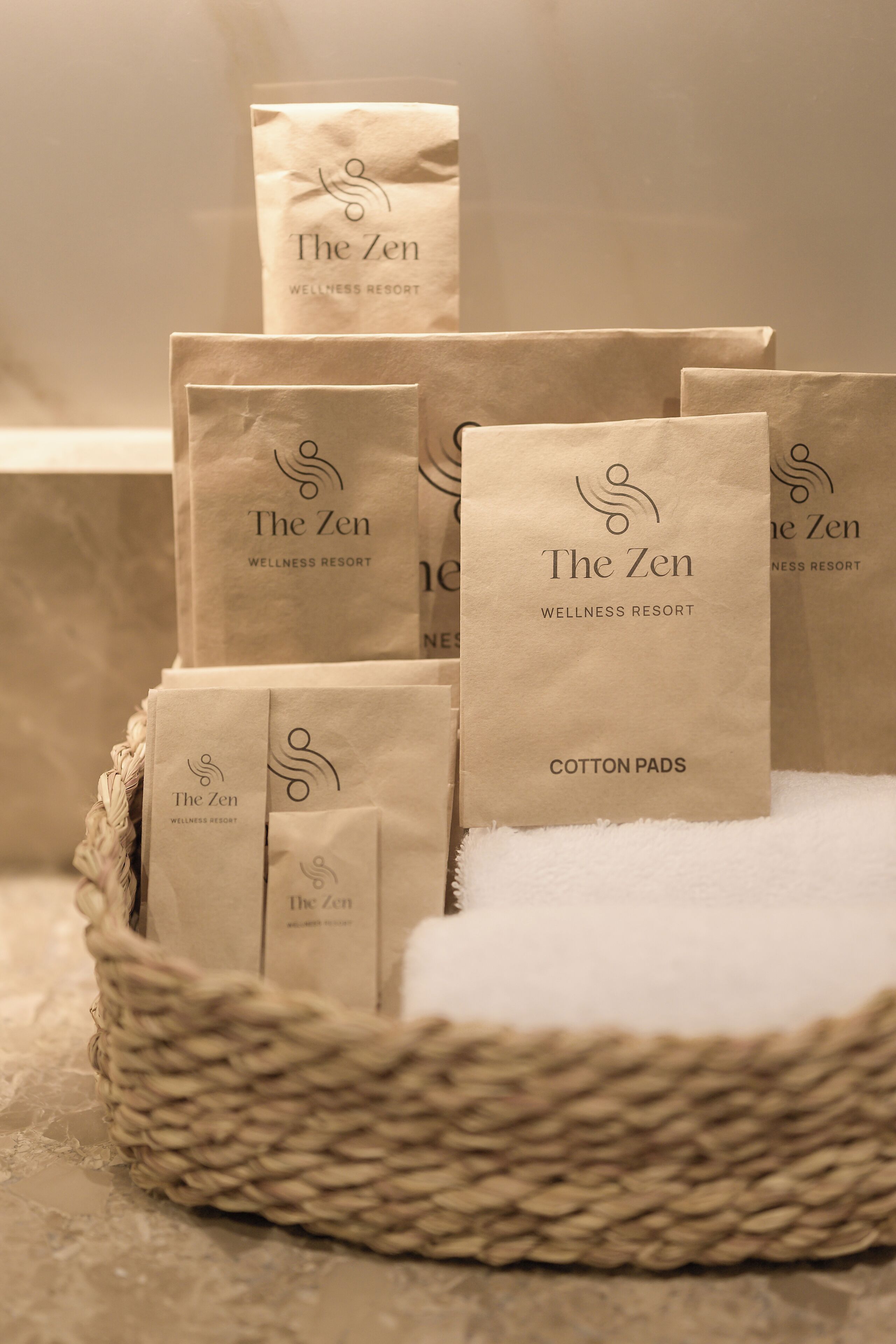 A basket containing several paper bags with "The Zen Wellness Resort" branding and "Cotton Pads" text.