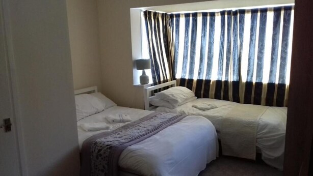 A room with two beds, a window with striped curtains, and a bedside table with a lamp. - Haven House Hotel (Southend-on-Sea)