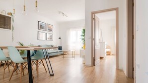 A spacious living area with a dining table, chairs, a sofa, and a coffee table. There are framed pictures on the wall, a plant, and a door leading to another room. - Clifftop Nest Arrifana by Lisbeyond (Aljezur)