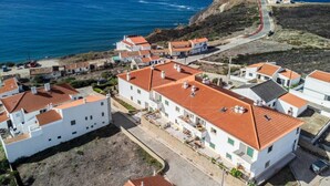A coastal village with white buildings and red roofs, a road leading to the sea, and a distant view of the ocean. - Clifftop Nest Arrifana by Lisbeyond (Aljezur)