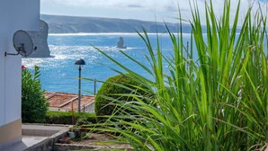 A coastal view with a white building, a rocky cliff, and a statue in the sea. - Clifftop Nest Arrifana by Lisbeyond (Aljezur)