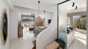 A modern bedroom with a curved wall, a large bed, a hanging light fixture, and a view of the outdoors.