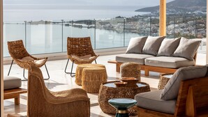 A modern living room with wicker furniture, a sofa, and ottomans, overlooking a scenic coastal view.