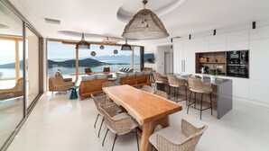 A modern kitchen with a central island, dining area with wicker chairs, and a large window overlooking a scenic view.