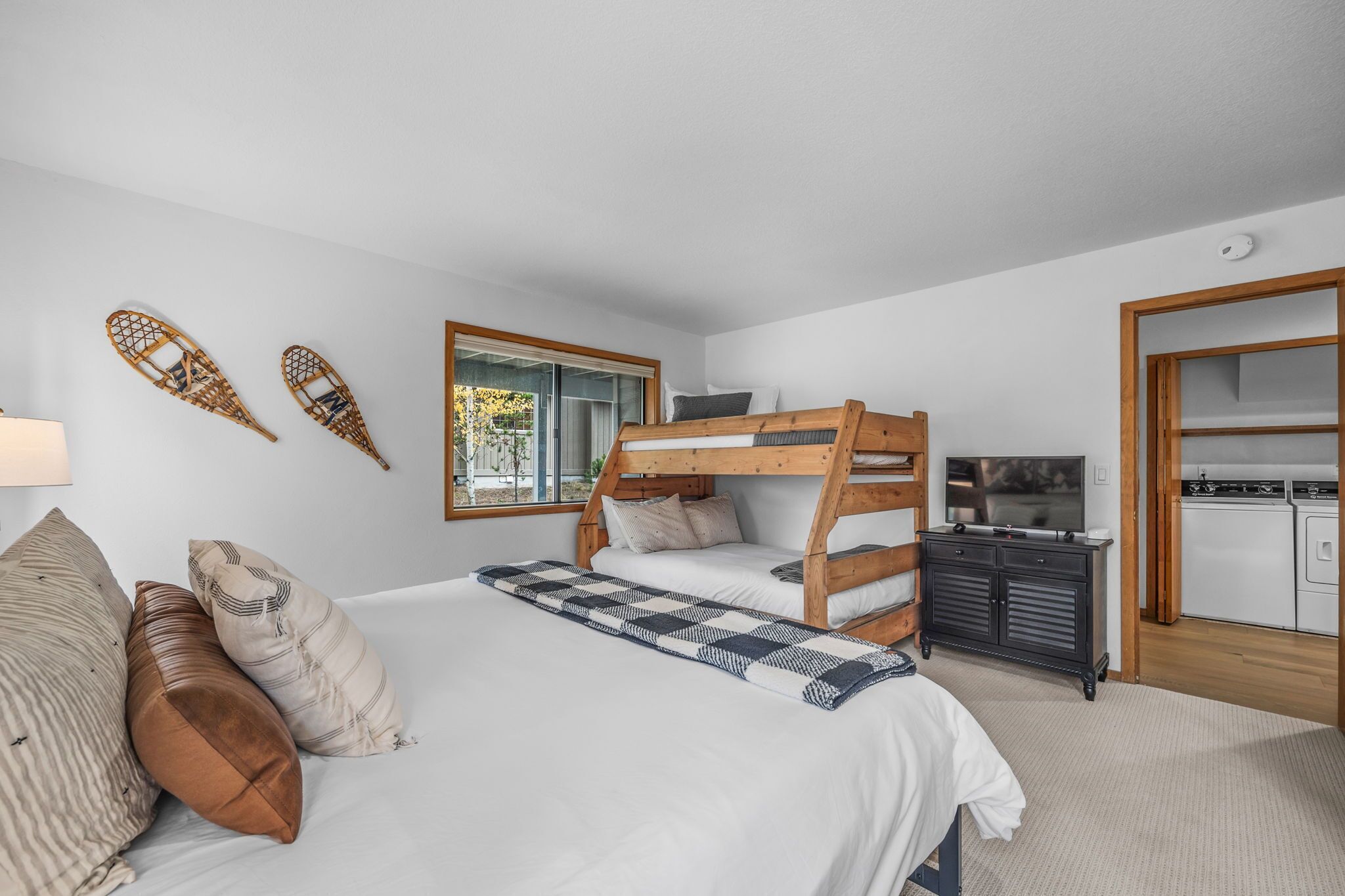A bedroom with a bunk bed, a desk with a TV, and a kitchen area.