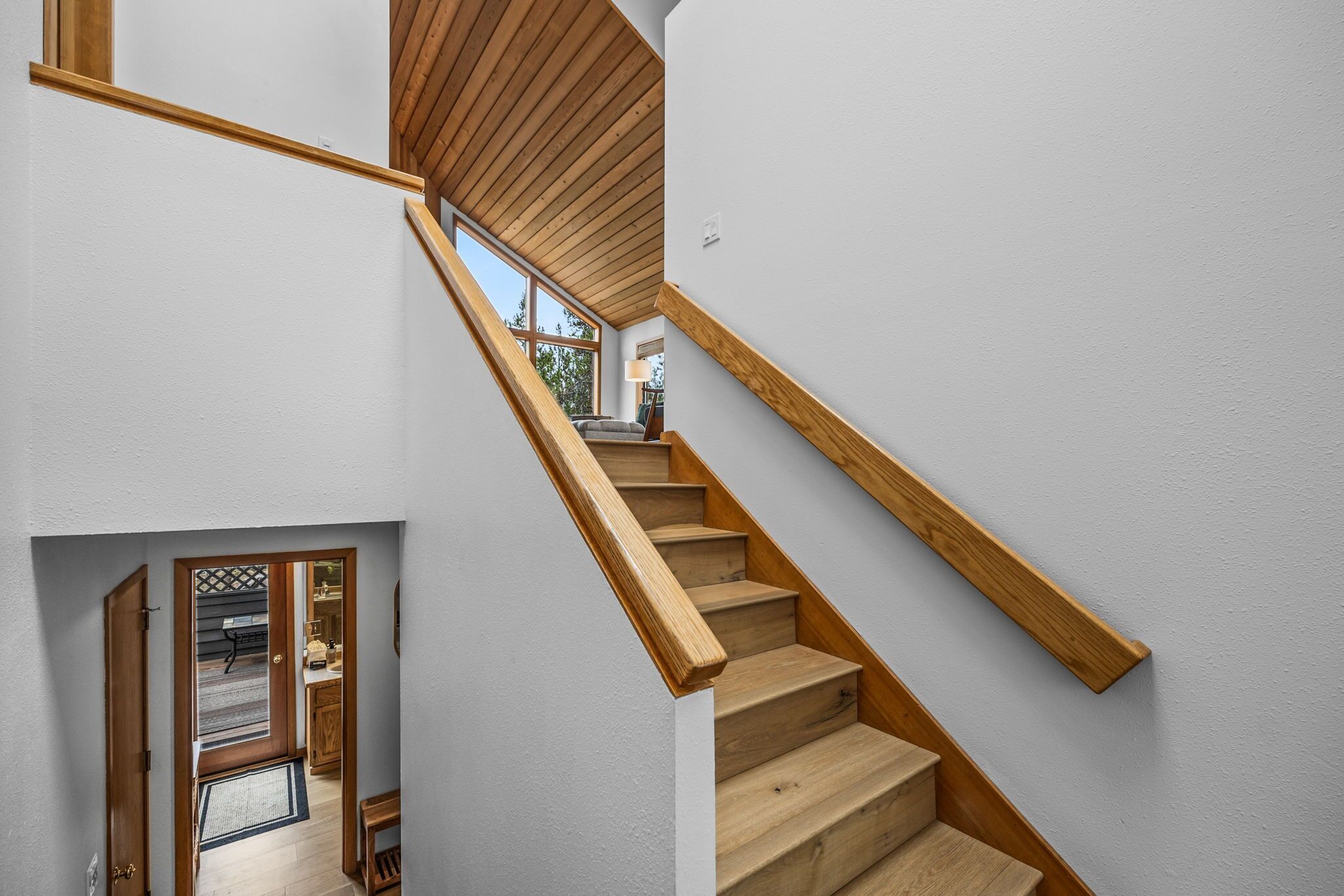 A wooden staircase with a view of a room and a door leading outside.