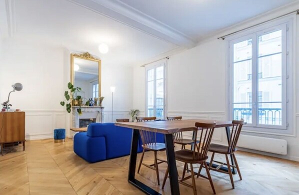 Ein geräumiges Zimmer mit einem Holzespeisetisch, einem blauen Sofa und einem großen Spiegel.