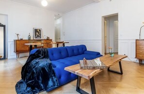 Ein Wohnzimmer mit einem blauen Sofa, einem Holztisch und einem schwarzen Samtstuhl.