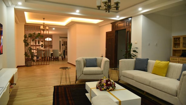A modern living room with a sofa, armchairs, a coffee table, and a dining area with chairs and a table. - 5 Bedroom Exquisite Villa in Top-view Area (Addis Ababa)