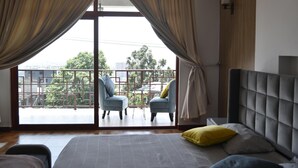 A bedroom with a bed, two armchairs, a balcony with a view of buildings and trees, and curtains. - 5 Bedroom Exquisite Villa in Top-view Area (Addis Ababa)
