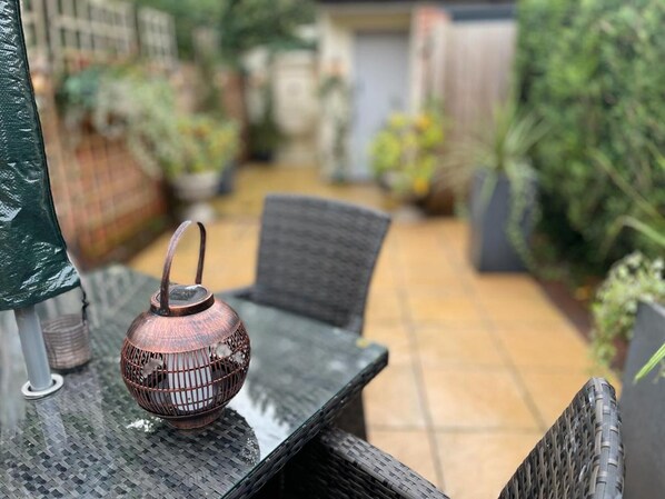 A patio with a wicker table and chairs, a copper teapot, and a green umbrella.