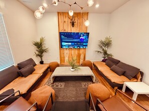 A modern living room with a flat-screen TV mounted on a wooden wall, a coffee table, sofas, and potted plants.