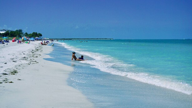 Una playa con agua turquesa cristalina, arena blanca y sombrillas.
