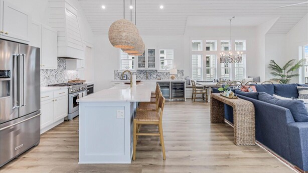 A modern kitchen with white cabinetry, a central island, and a dining area with wicker furniture. - Spacious, Pet-Friendly, Home w/Access to Pools &More Amenities Cinnamon Shore (Port Aransas)