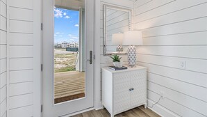 Een witte inrichting met een schuifdeur naar een terras, een wit kastje met decoratieve objecten, en een spiegel aan de muur.