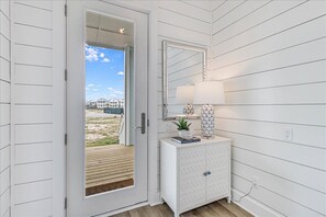 A white interior with a sliding glass door leading to a deck, a white cabinet with decorative items, and a wall-mounted mirror. - Spacious, Pet-Friendly, Home w/Access to Pools &More Amenities Cinnamon Shore (Port Aransas)