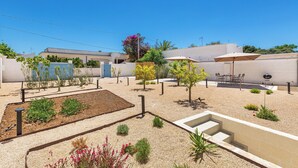 Un patio exterior bien cuidado con zona de barbacoa, mobiliario y diversas plantas.