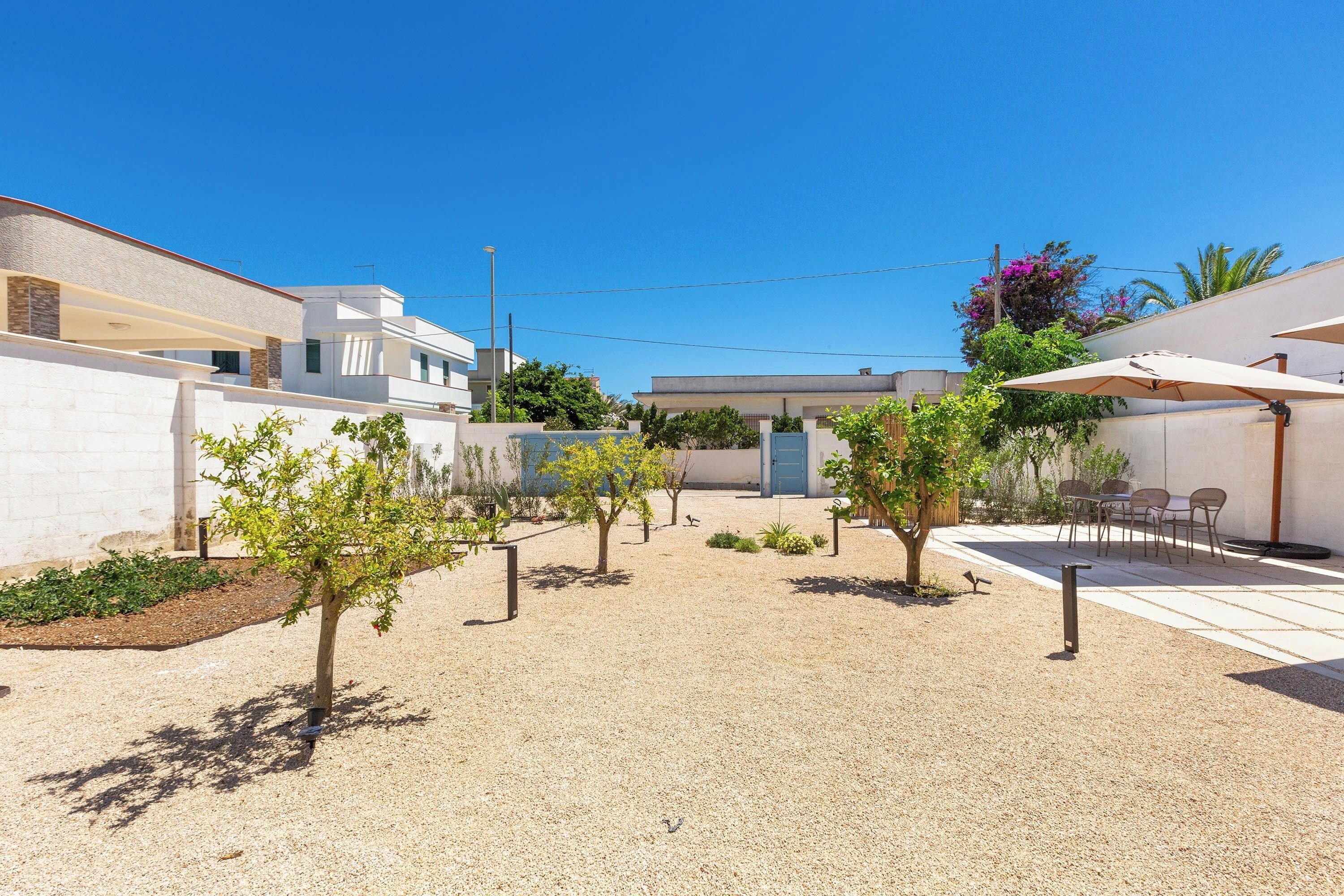 A courtyard with a gravel ground, small trees, outdoor seating, and a building with a blue door.