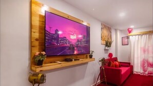 A modern living room with a large flat-screen TV mounted on a wooden shelf, a red sofa, a tripod, and a red carpet.