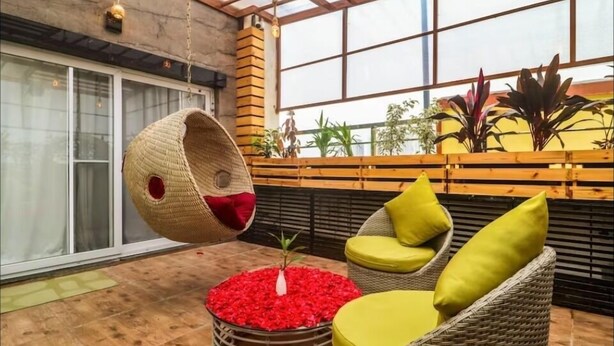 A cozy indoor seating area with wicker furniture, a hanging chair, and a small plant in a red flower pot.