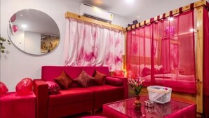 A red sofa with cushions, a round mirror, and a glass coffee table with a vase.