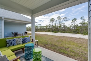 A covered outdoor seating area with a green sofa, patterned cushions, and a small table.