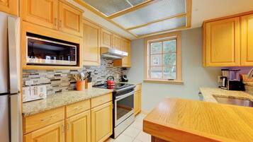 A kitchen with wooden cabinets, a microwave, a stove, and a window.