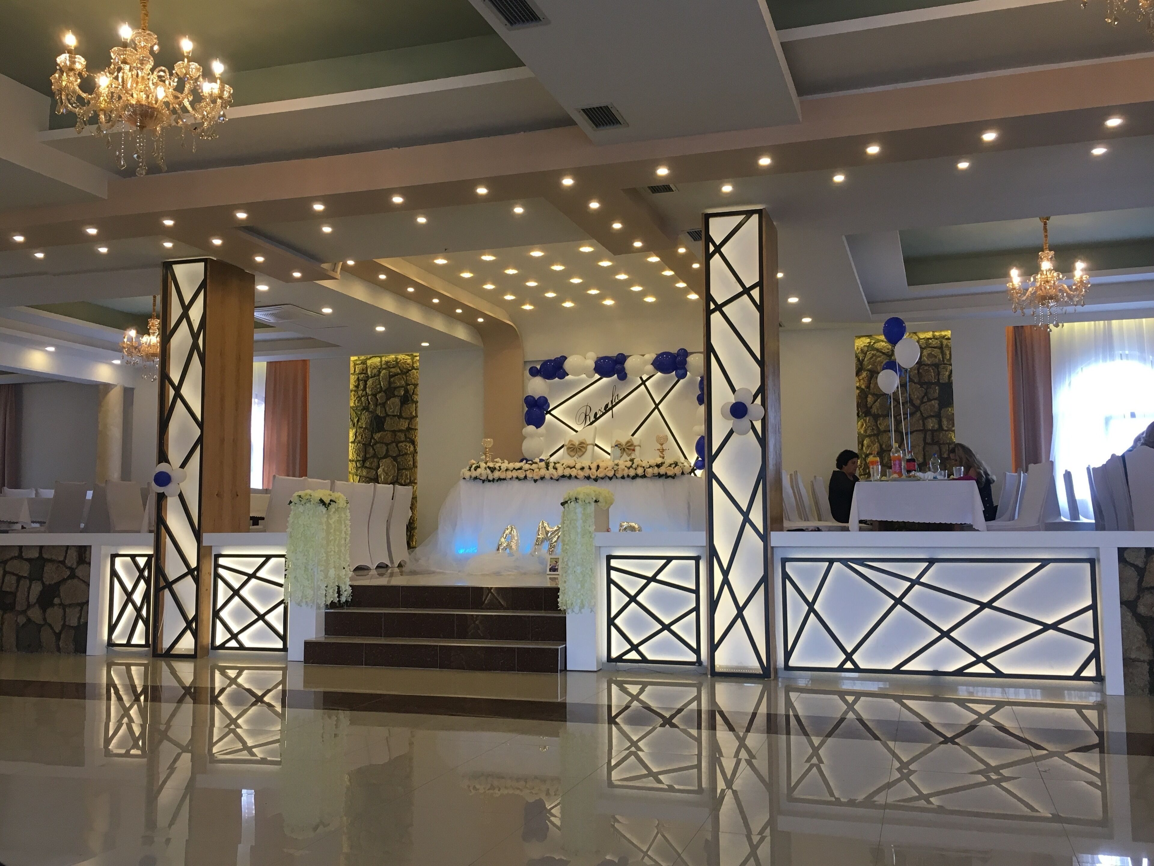 Un área de recepción bien iluminada con mostrador, pared decorativa con globos y una escalera que sube a un nivel superior.