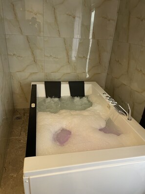 A bathtub with multiple jets, marble walls, and a tiled floor.