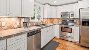 A modern kitchen with white cabinets, stainless steel appliances, and a tiled backsplash.
