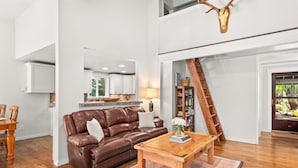 A spacious living room with a brown leather sofa, a wooden coffee table, and a dining area with a wooden table and chairs.