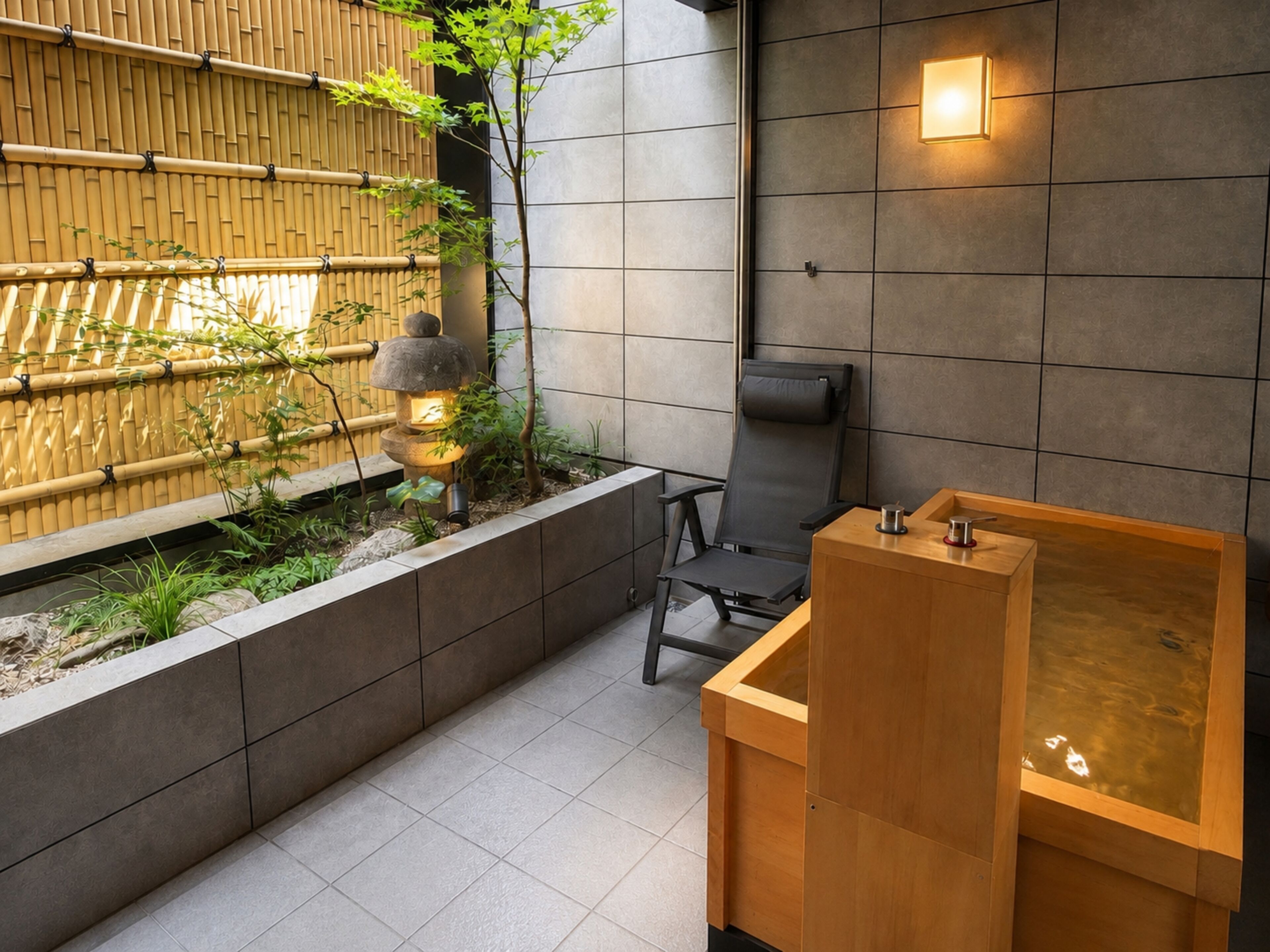 Un baño moderno con pared de bambú, una bañera de madera y una silla negra.