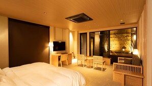 Une chambre d’hôtel dotée d’un grand lit, d’un bureau avec une télévision, d’un coin salon avec un canapé et des fauteuils, et d’une grande fenêtre donnant sur la forêt.