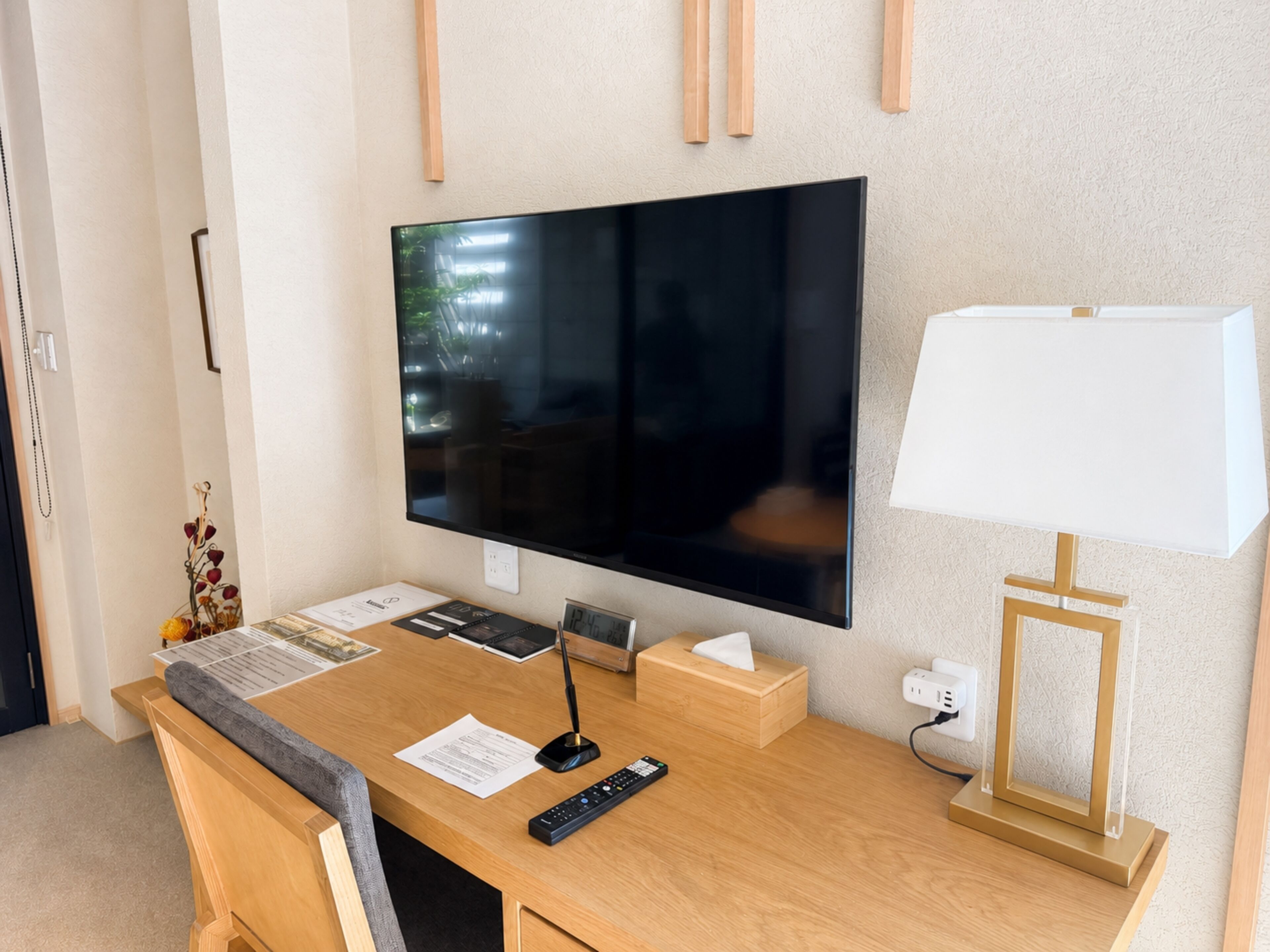 A hotel room with a wooden desk, a flat-screen TV, a lamp, and a power outlet.