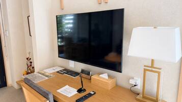 A hotel room with a wooden desk, a flat-screen TV, a lamp, and a power outlet.