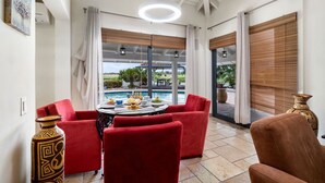 Ein Zimmer mit Blick auf einen Pool, rote Stühle, ein Tisch mit einer Vase und ein großes Fenster mit Vorhängen.