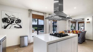 Eine moderne Küche mit einer zentralen Kochinsel, Edelstahlgeräten und Blick ins Freie.