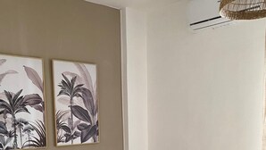 Una sala de estar moderna con un sofá color crema, una silla de madera y dos obras de arte colgantes que representan plantas tropicales.