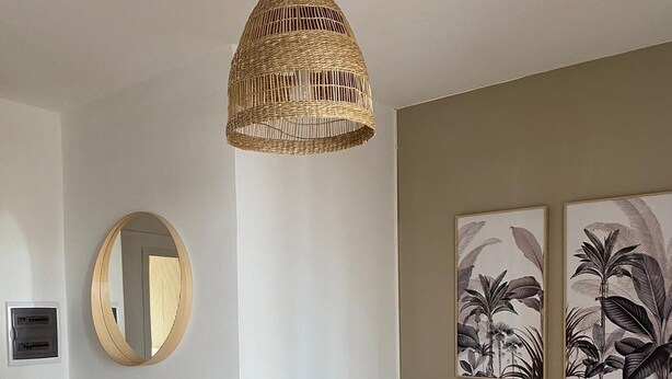 Una sala moderna con una mesa de comedor redonda, un sofá con cojines amarillos, una lámpara colgante de fibras naturales y dos impresiones botánicas enmarcadas en la pared.