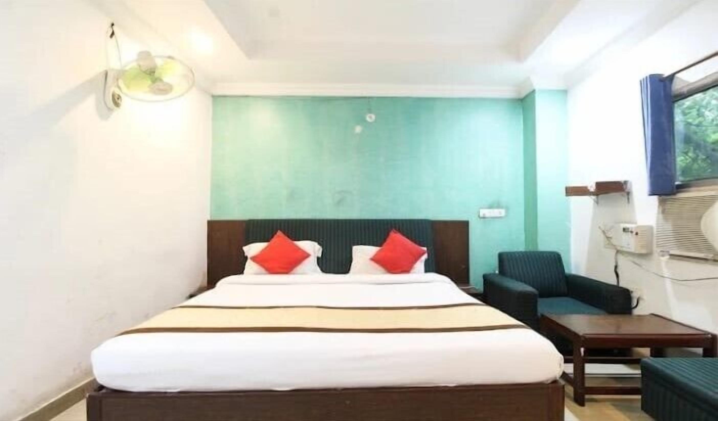 Habitación de hotel con cama, una silla, una mesita y aire acondicionado instalado en la pared.