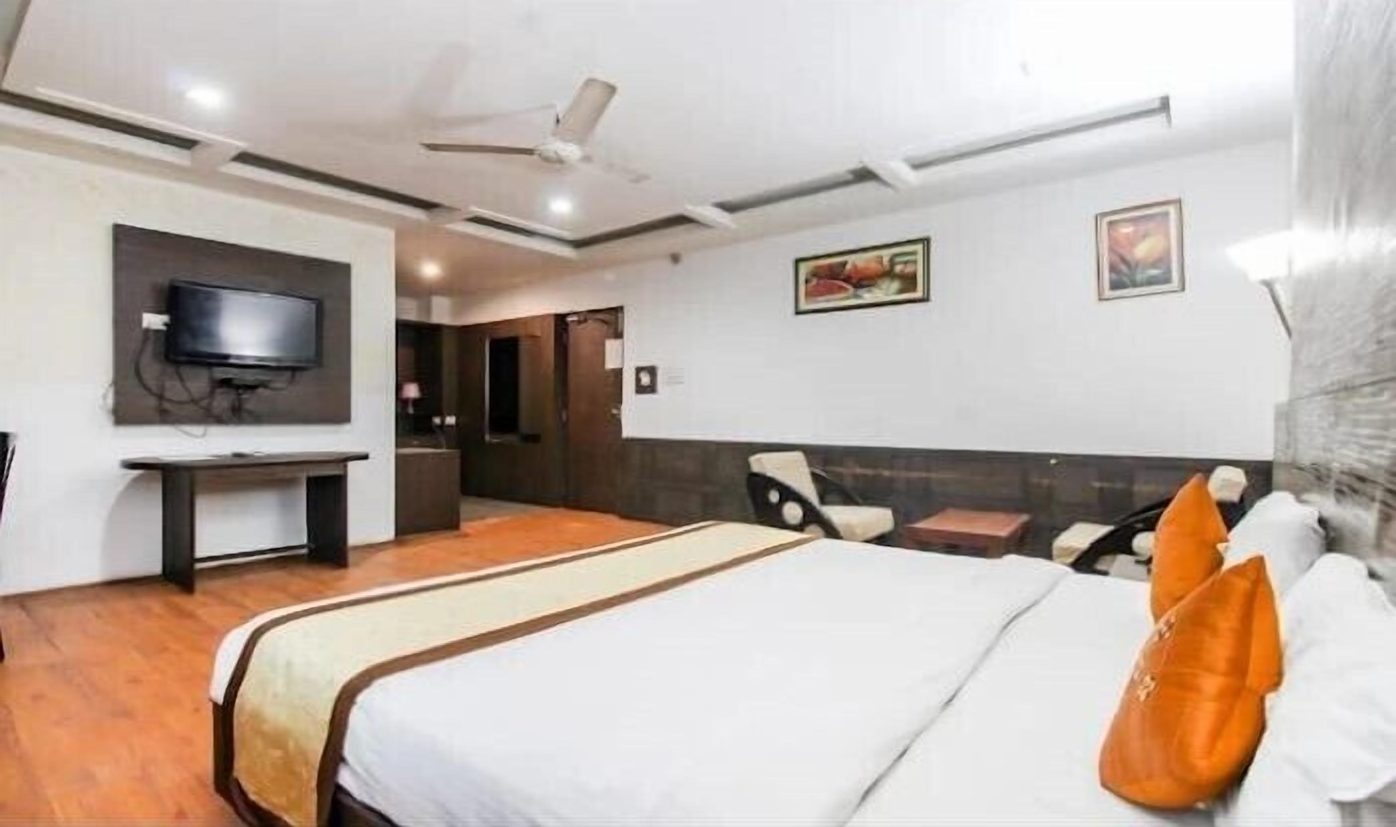 A hotel room with a bed, a desk, a television, and a ceiling fan.