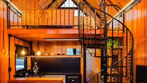 A cozy cabin interior with a wooden ceiling, a spiral staircase, a dining area, and a living room with a sofa and a cowhide rug. - Alta Vista Cabanas (Garibaldi)