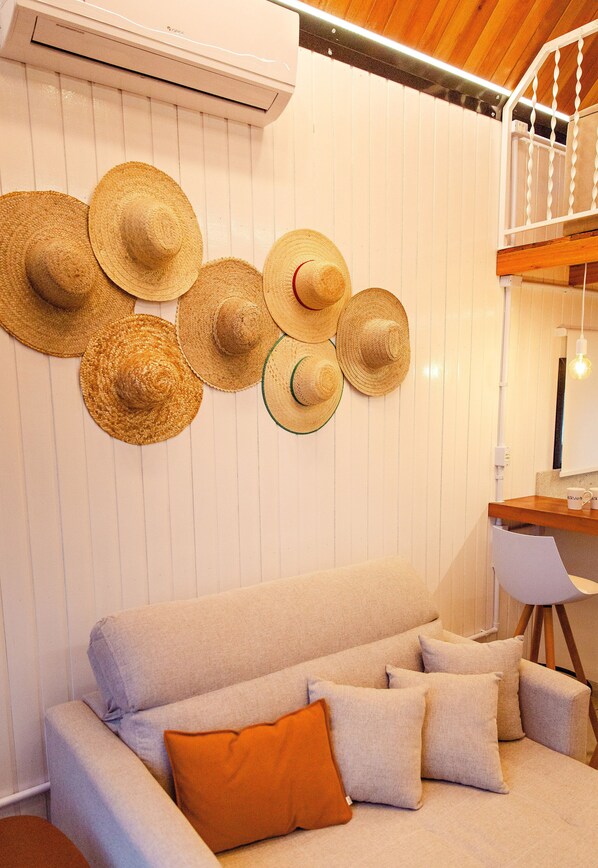 A room with a sofa, multiple hats on the wall, and an air conditioning unit.