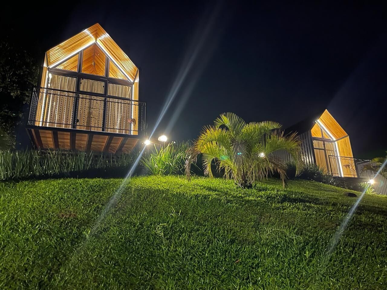 Due strutture in legno illuminate, dal design moderno, immerse nel verde di prati curati e palme.