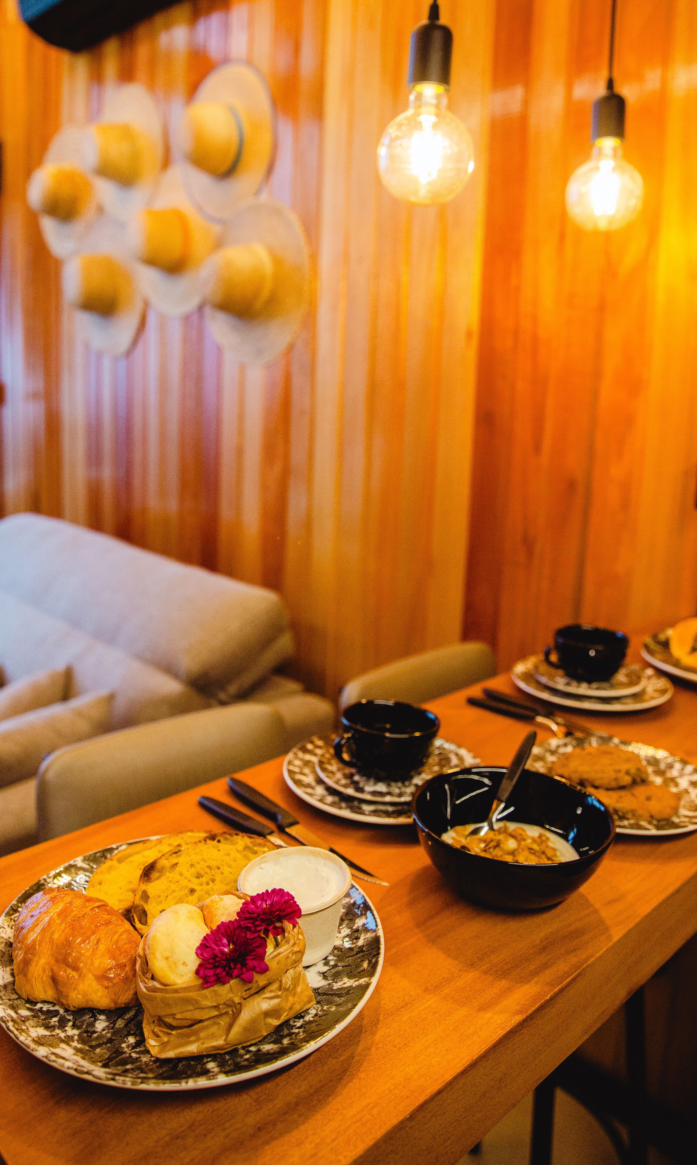 Un coin repas avec une table en bois mise pour un repas, comprenant des assiettes remplies de nourriture et des bols noirs.