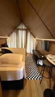 Quarto compacto em formato triangular, com uma cama, escrivaninha, cadeira e televisão.