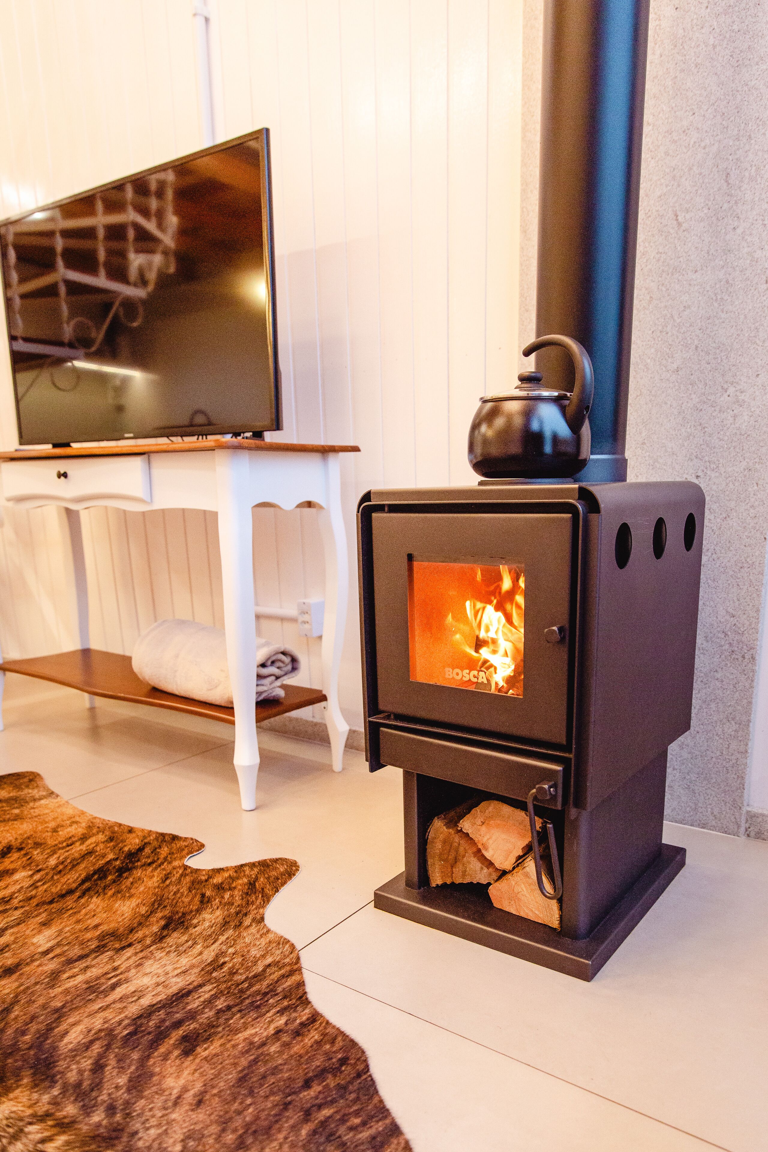 A modern living room with a wood-burning stove, a television on a white cabinet, and a brown rug on the floor.