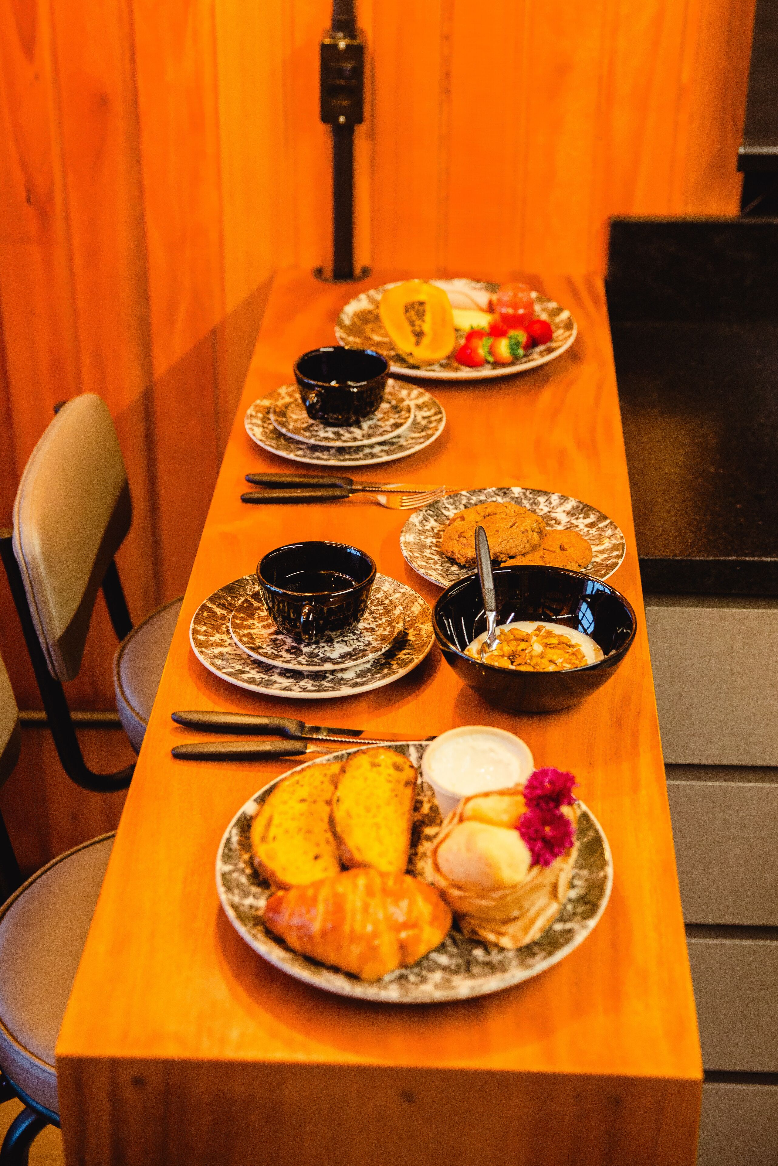 A wooden dining table with plates of food, bowls, and cutlery.