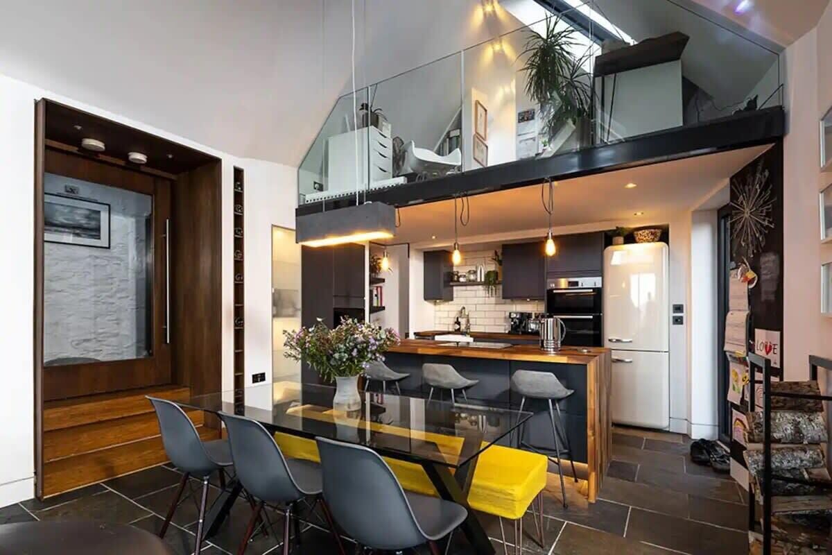 A modern kitchen with a glass dining area, a central island, and a staircase leading to an upper level.